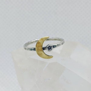 May include: A silver ring with a hammered texture and a gold crescent moon charm with a black star in the center.