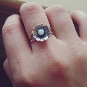 May include: A silver ring with a flower design and an opal gemstone in the center.