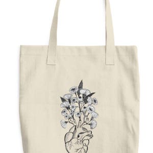 May include: A beige tote bag with a black and white illustration of a human heart with flowers growing out of it.