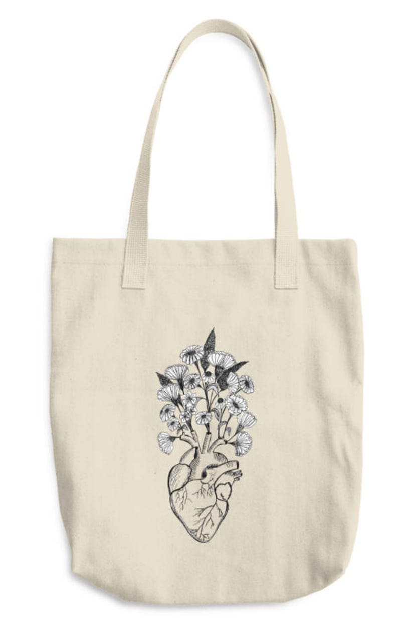 May include: A beige tote bag with a black and white illustration of a human heart with flowers growing out of it.