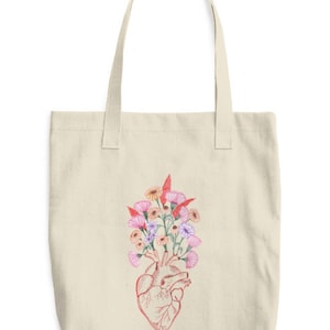 May include: A beige tote bag with a red anatomical heart design with colorful flowers growing out of it.