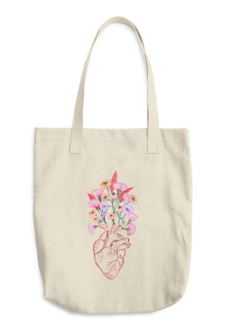 May include: A beige tote bag with a red anatomical heart design with colorful flowers growing out of it.