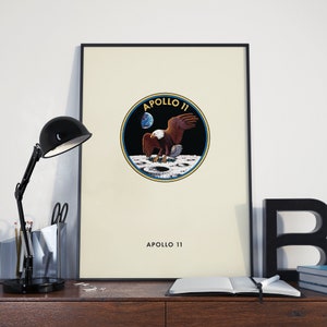 May include: A black and white poster with a yellow circle in the centre. The circle contains a graphic of an eagle landing on the moon with the Earth in the background. The text "APOLLO 11" is written above the circle and below the circle.