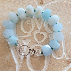 May include: A light blue gemstone bracelet with a silver toggle clasp. The bracelet is made of faceted aquamarine beads and small dark blue spacer beads.