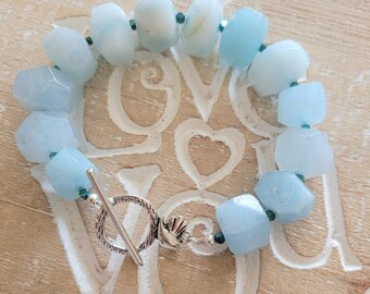May include: A light blue gemstone bracelet with a silver toggle clasp. The bracelet is made of faceted aquamarine beads and small dark blue spacer beads.