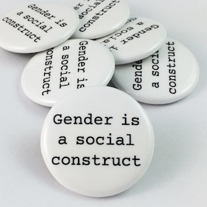 May include: A close-up of several white round buttons with the text "Gender is a social construct" printed in black.