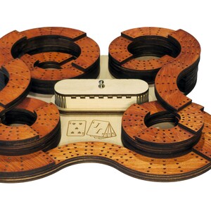 May include: A wooden cribbage board with four circular tracks and a central compartment for cards. The board is made of layered wood with a reddish-brown finish. The board is designed for playing the card game cribbage.
