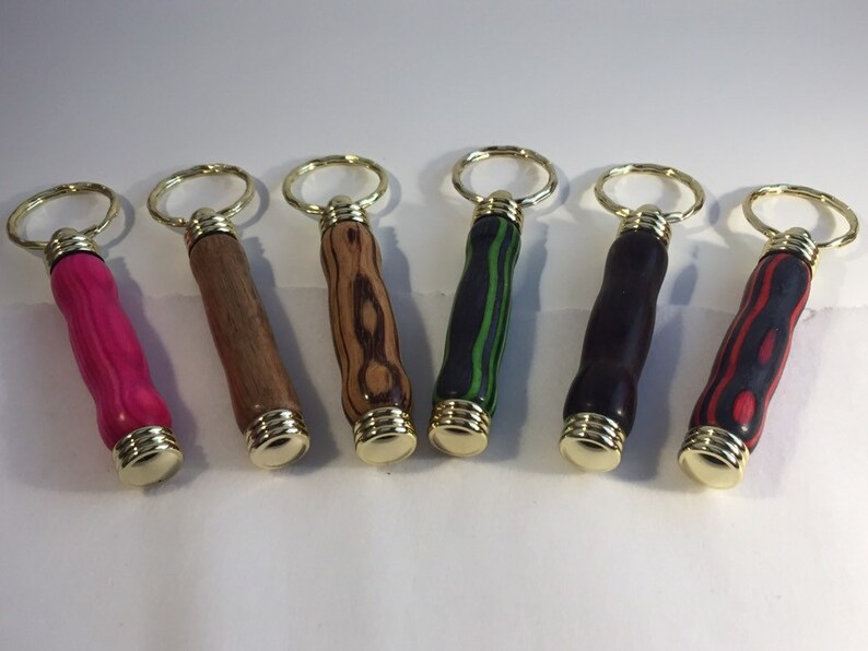 May include: Six wooden keychain bottle openers with different wood grain patterns and colors. The keychains are gold colored metal.