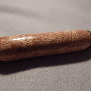 May include: A wooden keychain with a brown and pink wood grain pattern and gold metal accents.