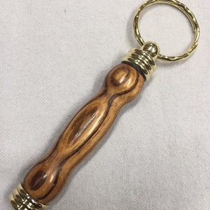 May include: A wooden keychain with a gold metal ring and a brown wood handle. The handle has a wood grain pattern.