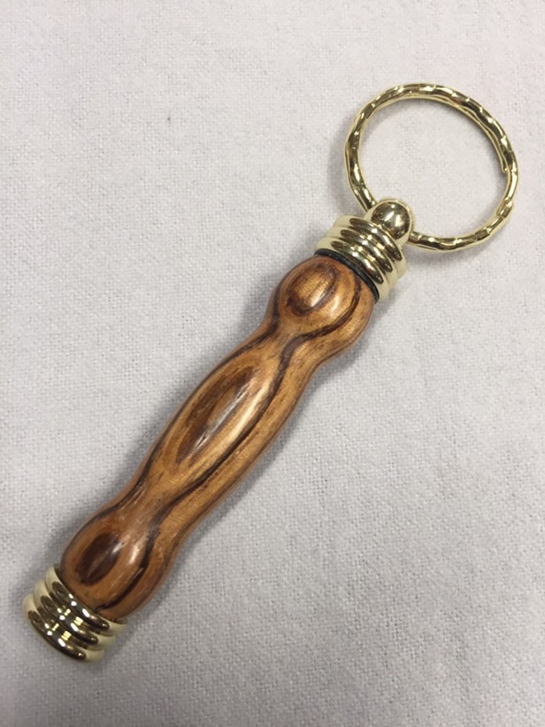 May include: A wooden keychain with a gold metal ring and a brown wood handle. The handle has a wood grain pattern.