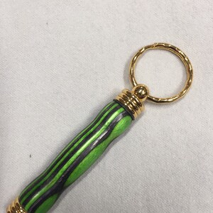 May include: A green and black wooden keychain with a gold ring and gold accents.