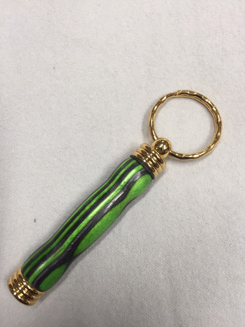 May include: A green and black wooden keychain with a gold ring and gold accents.