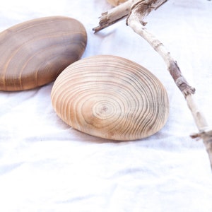 May include: Four wooden coasters with a natural wood finish. The coasters are round and oval shaped and have a smooth surface. The coasters are arranged on a white fabric background.
