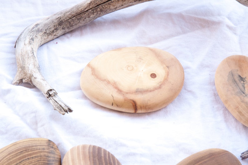 May include: Four wooden coasters in various shades of brown, with a natural wood grain pattern. The coasters are oval shaped and have a smooth, polished finish.