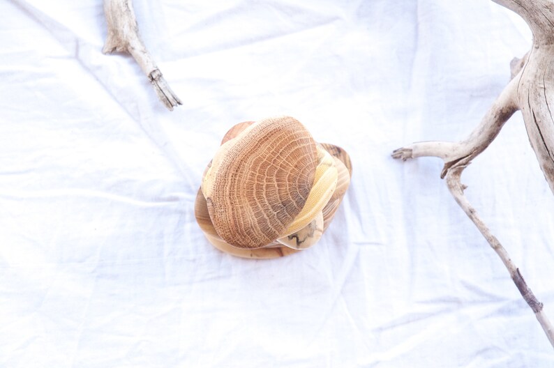 May include: A set of three wooden bowls stacked on top of each other. The bowls are made of light brown wood with a natural grain pattern. The bowls are round and have a slightly curved shape.