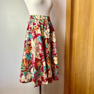 May include: A red, green, and white floral midi skirt with a button closure. The skirt is on a white mannequin.