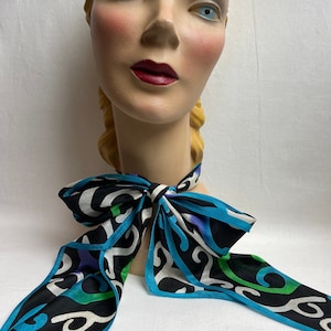 May include: A mannequin head with blonde hair wearing a black and white patterned scarf with turquoise, green, and purple accents.