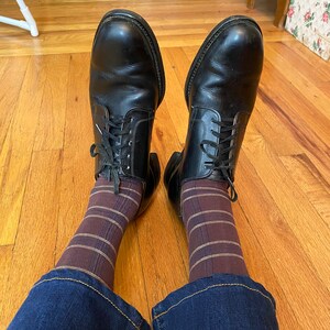 May include: A pair of black leather lace-up shoes with brown and gold striped socks and blue jeans.