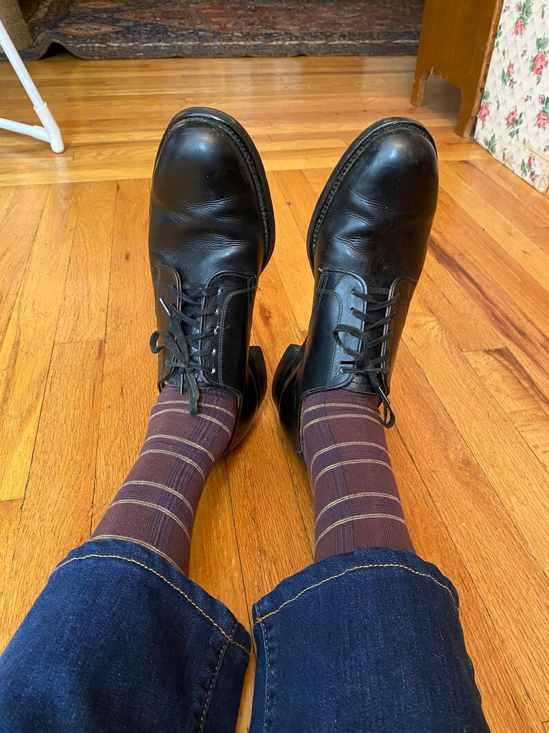 May include: A pair of black leather lace-up shoes with brown and gold striped socks and blue jeans.