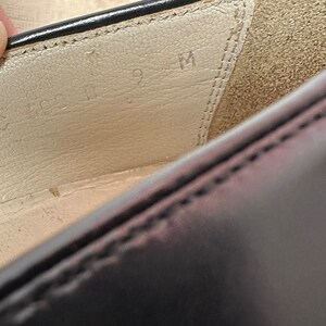 May include: Close-up of the inside of a black leather shoe. The insole is white and has the size "9 M" written on it.