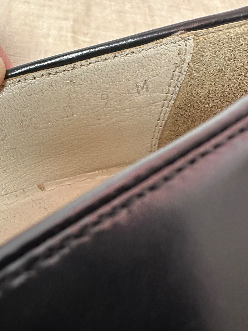 May include: Close-up of the inside of a black leather shoe. The insole is white and has the size "9 M" written on it.