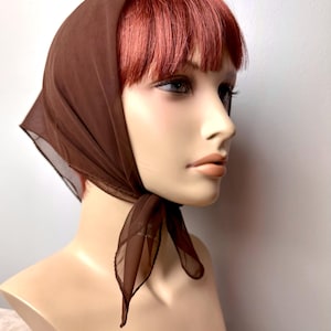 May include: A brown sheer headscarf tied in a knot at the nape of the neck. The scarf is made of a lightweight, flowing fabric.