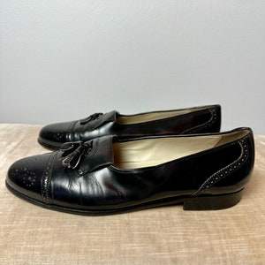 May include: A pair of black leather tassel loafers with a brogue design. The shoes have a pointed toe and a low heel.