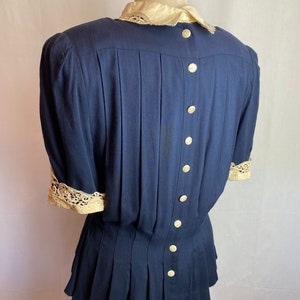 May include: A navy blue blouse with a white lace collar and cuffs. The blouse has a pleated skirt and a button-up back.