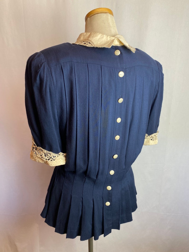 May include: A navy blue blouse with a white lace collar and cuffs. The blouse has a pleated skirt and a button-up back.