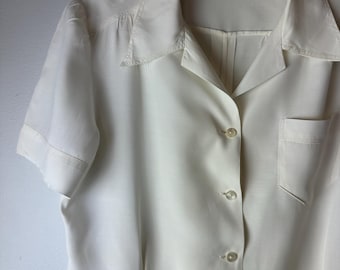 May include: A white button-down shirt with short sleeves and a pocket on the left side. The shirt has a collar and is made of a smooth fabric.