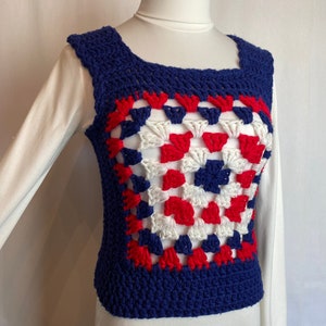 May include: A crocheted vest with a square pattern in red, white and blue. The vest is sleeveless and has a square neckline.