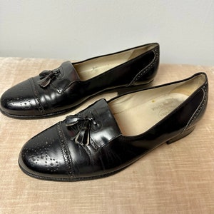 May include: A pair of black leather tassel loafers with a brogue design. The shoes have a pointed toe and a low heel.