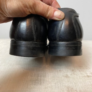 May include: A pair of black leather dress shoes with a stitched seam detail on the back of the heel.