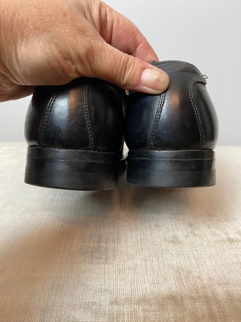 May include: A pair of black leather dress shoes with a stitched seam detail on the back of the heel.