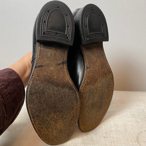 May include: A pair of black leather shoes with brown leather soles. The shoes have a classic design and are in good condition.
