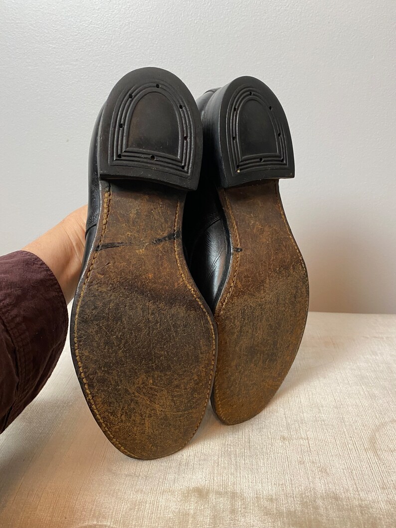 May include: A pair of black leather shoes with brown leather soles. The shoes have a classic design and are in good condition.
