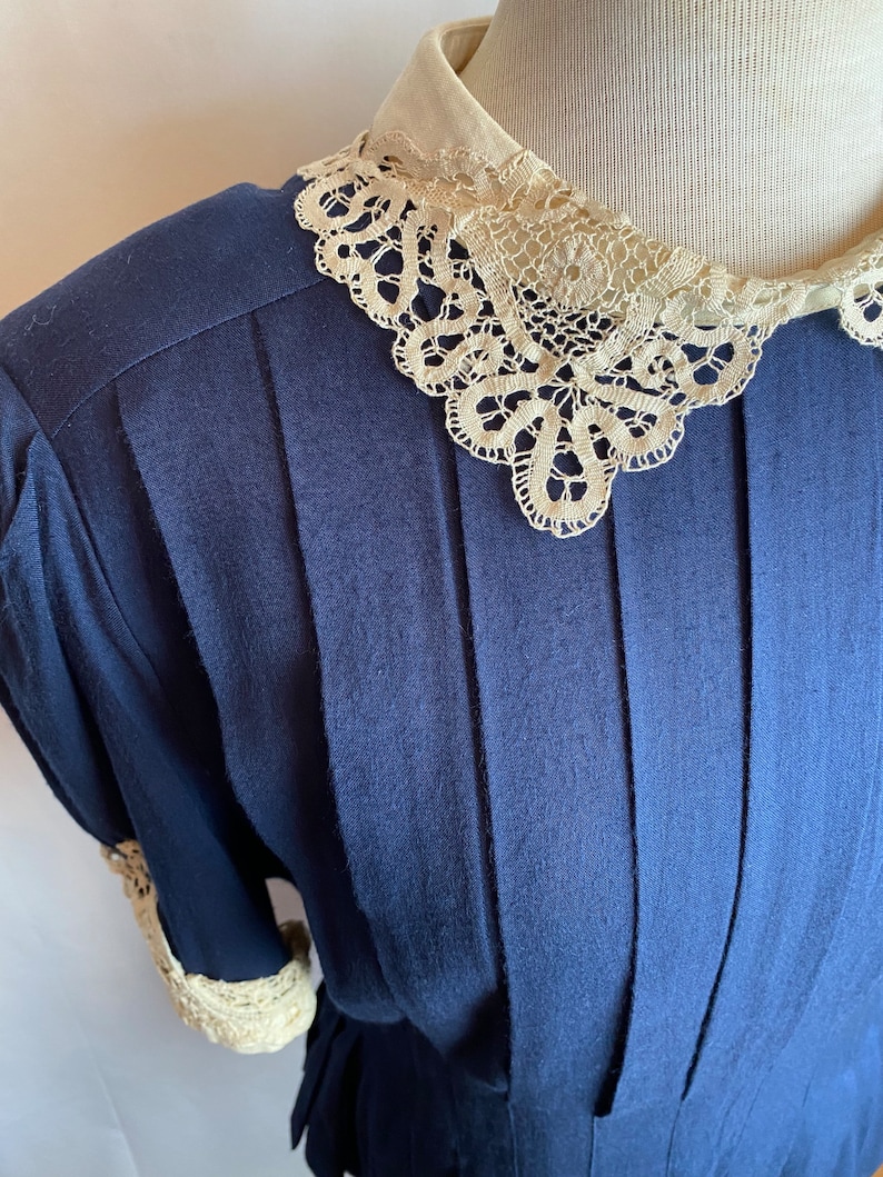 May include: A navy blue dress with a white lace collar and cuffs. The dress has a pleated bodice and a fitted waist.