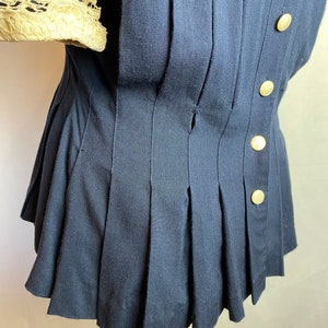 May include: A navy blue blouse with a pleated skirt and gold buttons. The blouse has a lace trim on the sleeves.