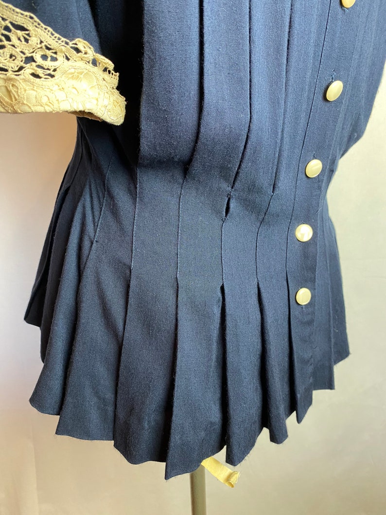 May include: A navy blue blouse with a pleated skirt and gold buttons. The blouse has a lace trim on the sleeves.