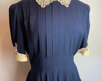 May include: A navy blue blouse with a white lace collar and cuffs. The blouse has a fitted bodice and a flared skirt.