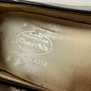 May include: Close-up of the inside of a shoe with a cream-colored leather insole. The insole has the text "HANDMADE" and "CREATED EXCLUSIVELY FOR CLASSICS" in a circular design. The text "PRIMA CLASSE" is printed below the circle.