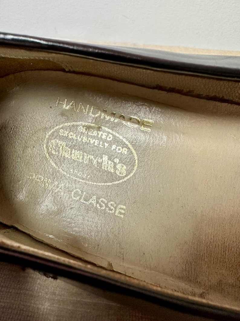 May include: Close-up of the inside of a shoe with a cream-colored leather insole. The insole has the text "HANDMADE" and "CREATED EXCLUSIVELY FOR CLASSICS" in a circular design. The text "PRIMA CLASSE" is printed below the circle.