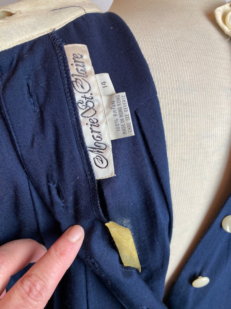 May include: A navy blue dress with a white collar and a white label that says "Monique St. Claire" and "100% Rayon Made in Hong Kong Care See Reverse 14".