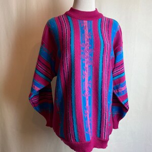 May include: A pink, blue, and purple striped sweater with a floral pattern. The sweater has a crew neck and long sleeves.