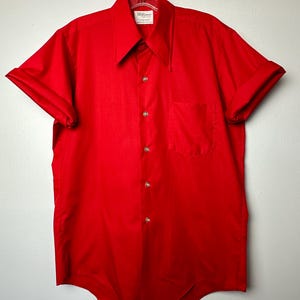 May include: A red short-sleeved button-down shirt with a pointed collar. The shirt has a single chest pocket and a brand label that reads "Williams Fashionwear"