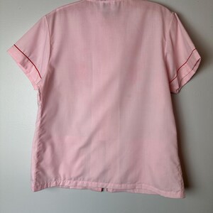 May include: A pink short-sleeved button-up shirt with red trim around the collar and sleeves.