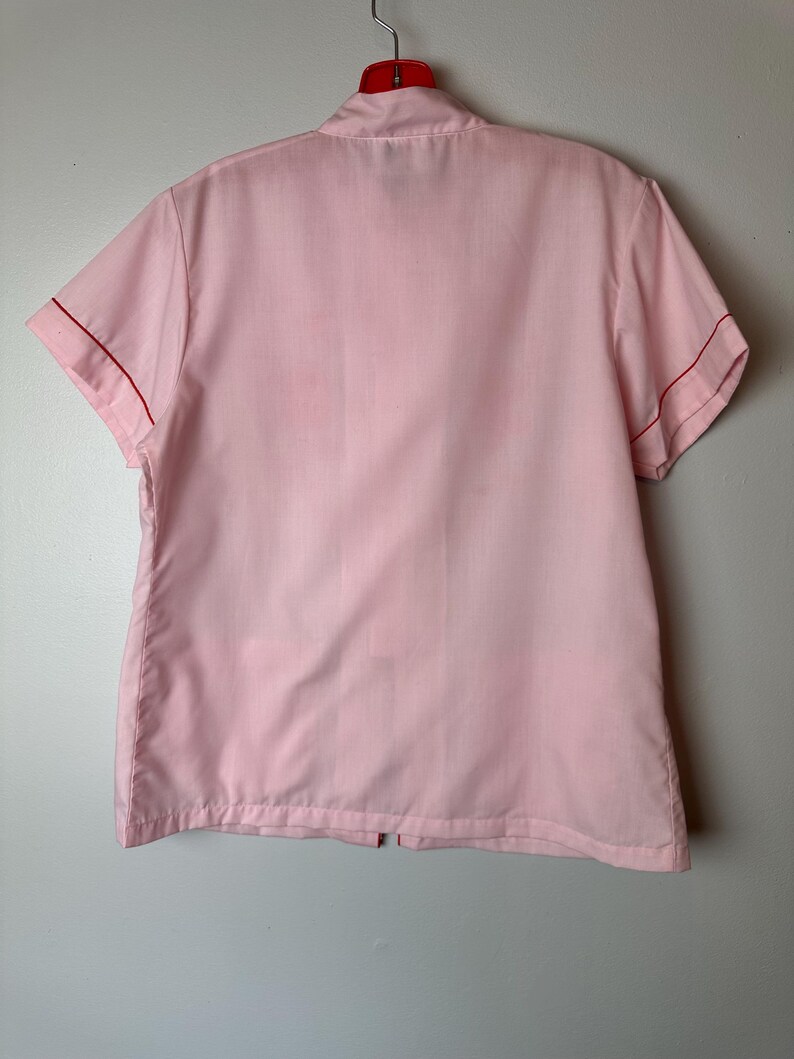 May include: A pink short-sleeved button-up shirt with red trim around the collar and sleeves.