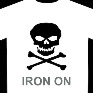 以下が含まれることがあります： 胸の中央にスカルとクロスボーンの黒いグラフィックが描かれた白いTシャツ。スカルとクロスボーンの下には、太字のグレーのサンセリフフォントで「IRON ON」という文字がプリントされています。Tシャツには黒い袖が付いています。