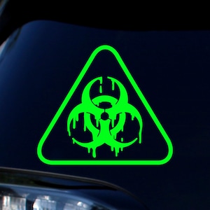 May include: A neon green biohazard symbol with a dripping effect inside a green triangle. The symbol is a warning sign, often associated with hazardous materials or biological threats. The design is a sticker or decal.